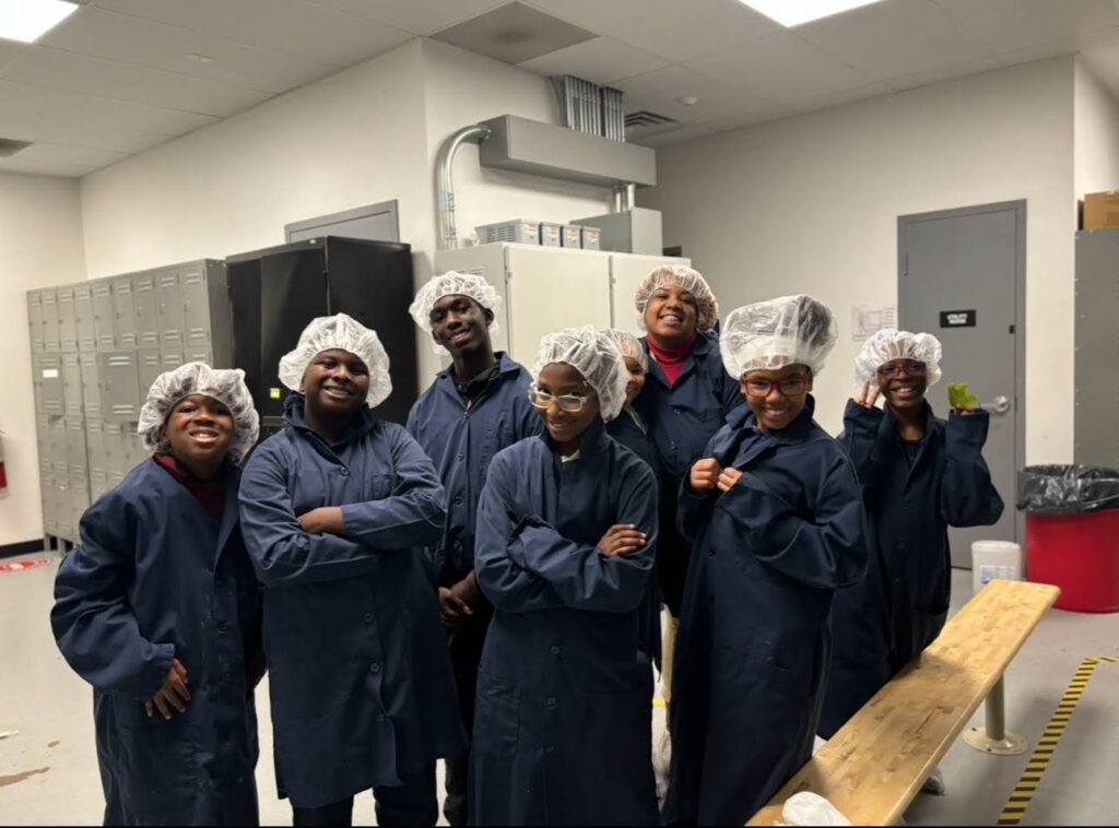 Chala's students posing while dressed in PPE with hairnets and lab coats getting ready for a tour