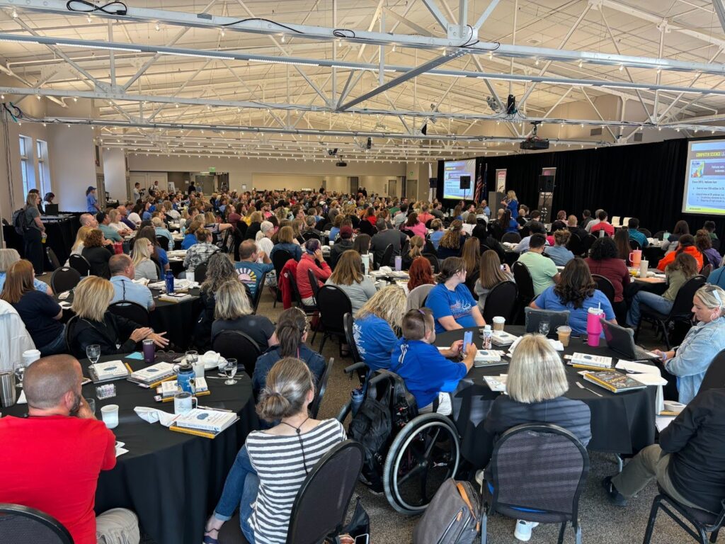 CSPDWeek Gathering showing hundreds of people in a room, facing the presentation at the front.