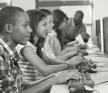 A line of students sit at a row of computers. 