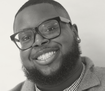 Headshot of Donald Saint-Germain, a black man with a close cropped fade, full beard, black framed glasses and stud earrings