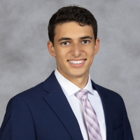 Maurice Korish is a young man with medium-light skin, short brown hair and brown eyes. He wears a navy suit jacket and pink tie as he smiles at the camera.